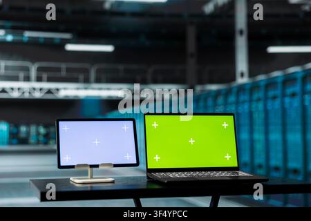 Green screen laptop and tablet overseeing data center hardware rackmounts driving automation tasks. Mockup devices in server room used to do backup of sensitive customers data Stock Photo
