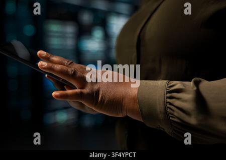 Close up of programmer using touchscreen device to do maintenance in data center with setup helping companies stay connected. IT expert walks with tablet between server hub machines blinking lights Stock Photo