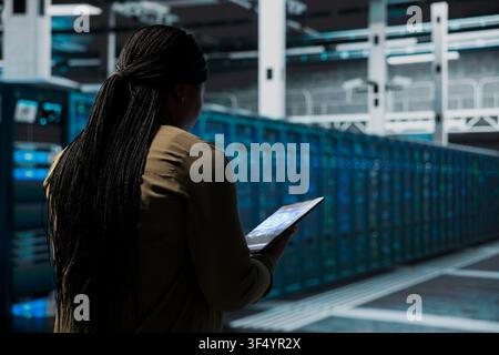 Computer scientist uses AI to do checkup on data center electronics processing datasets. Woman in server room uses deep learning to do backup on gear used by cloud storage hosting companies Stock Photo