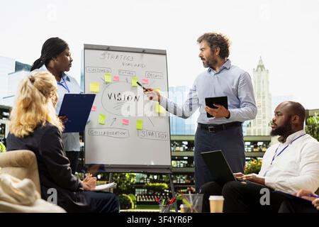 Diverse business team pointing toward vision roadmap on whiteboard, hosting informal meeting for strategy presentation. Collaborative discussion between colleagues. Stock Photo