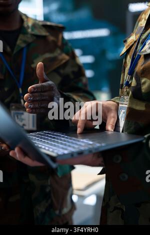 Close up shot of military soldiers using laptop in command post headquarters. Army specialists inputting mission data on notebook device, working together Stock Photo