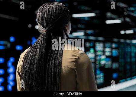 Engineer doing maintenance in data center with setup helping companies stay connected. Worker walking in server farm rows with machines blinking lights showing system activity Stock Photo