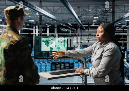 Team of military experts in data center reviewing geopolitical data on digital map interface. Female army information specialist and and commander in server farm analyzing worldwide threat indicators Stock Photo