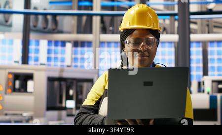 Solar panels factory engineer analyzing data from IoT sensors to refine equipment operational efficiency. Worker performing system diagnostics to reduce downtime in photovoltaic production, camera B Stock Photo