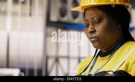 Engineer in smart solar manufacturing facility calibrating high tech machinery and analyzing sensor data. Engineer troubleshooting photovoltaic assembly equipment, camera B close up Stock Photo