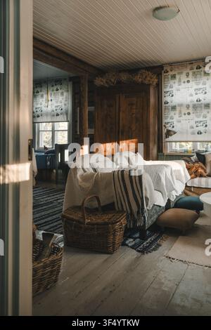 Laane County, Estonia - 17 May 2024: View of a cozy, sunlit interior in Vormsi featuring rustic wooden walls, white-covered armchairs, a wicker basket Stock Photo