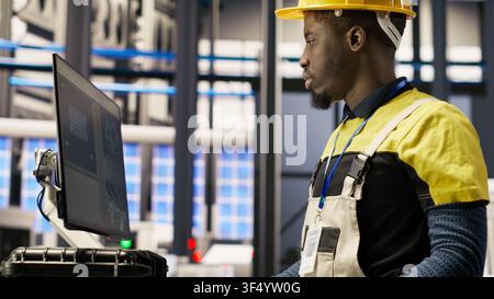 Solar panels plant engineer uses PC to oversee systems, ensuring machinery operates at optimal efficiency. Photovoltaics plant worker uses computer software to maintain continuous operations, camera B Stock Photo