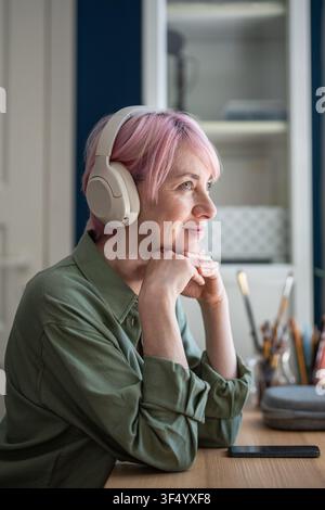 Cheerful woman in headphones enjoying listening to online podcasts or music playlist on smartphone. Stock Photo