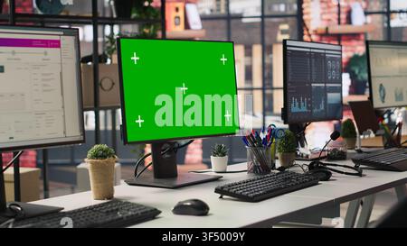 Chroma key computer displays in empty office showing analytics dashboards and data graphs. Office workspace with green screen PCs showing digital data visualization, panning shot Stock Photo