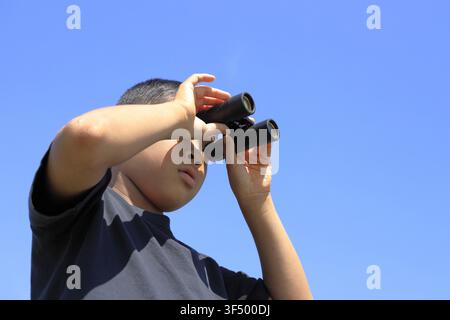 Japanese boy with opera glass under the blue sky (10 years old) Stock Photo