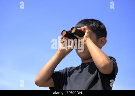 Japanese boy with opera glass under the blue sky (10 years old) Stock Photo