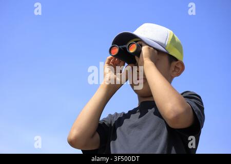 Japanese boy with opera glass under the blue sky (10 years old) Stock Photo