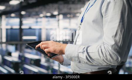 Programmers on data center industrial platform checking code on tablet, doing software updates. Server farm IT professionals cooperating, finetuning rackmounts configurations Stock Photo