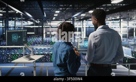 Data center team on industrial platform collaborating to maintain servers using artificial intelligence. Engineers cooperating to support infrastructure AI machine learning automatization, Stock Photo