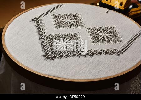 A close-up of traditional drawn thread embroidery in progress on natural linen fabric stretched in a wooden embroidery hoop. The intricate geometric o Stock Photo
