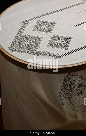 A traditional drawn thread embroidery project on fine linen fabric stretched in a large wooden embroidery hoop. The intricate geometric openwork patte Stock Photo