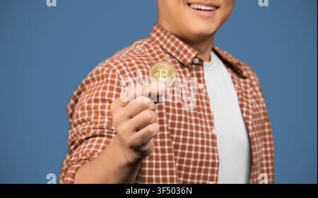 Happy Asian Man Holding Bitcoin Coin Smiling, Blue Background, Cryptocurrency Concept Stock Photo