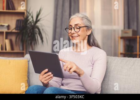 Smiling Elderly Woman Using Tablet At Home, Enjoying Technology And Connection Stock Photo
