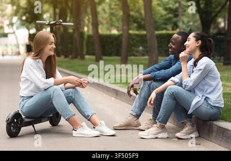 Three Young Adults Smiling And Chatting Outside In Park, Casual Outdoor Lifestyle Stock Photo