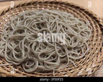 Spiralized soba noodles rest softly on a woven bamboo tray. Light dusting of steam hints at warmth and freshness. The texture invites a gentle bite, c Stock Photo