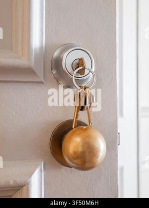 A bunch of brass keys inserted into a stainless steel deadbolt lock above a round satin brass doorknob on an open residential entrance door. Stock Photo