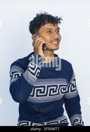 A cheerful young South Asian man with curly hair and a mustache enjoys a phone conversation Stock Photo