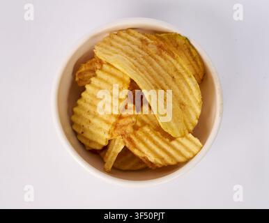 Top view of ridged potato chips in a ceramic bowl isolated on white background Stock Photo