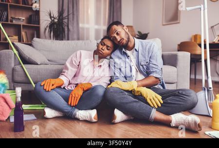Couple Cleaning Together At Home, Black Man And Woman Feeling Exhausted, Relaxed Lifestyle Stock Photo