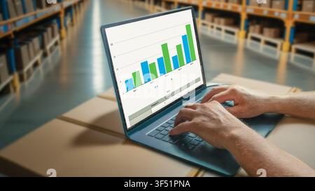 Close-up of a worker using a laptop displaying inventory analytics and bar charts inside a modern warehouse. Concept of logistics, supply chain manage Stock Photo