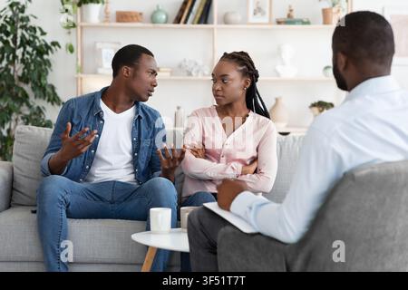 Young Black Spouses Having Relationship Problems, Sitting At Therapy Session With Counselor Stock Photo