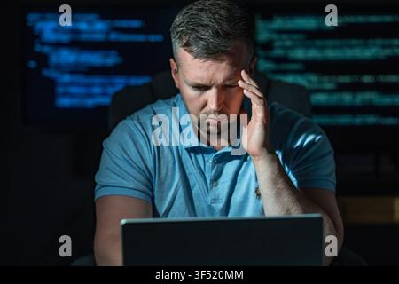 Cyber crime hacker works in darkness. Cyber crime hacker uses laptop computer. Cyber crime hacker accesses secure network. Cyber crime hacker steals Stock Photo