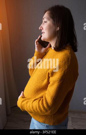 Pregnant woman holding a phone and smiling in a warm indoor setting Stock Photo