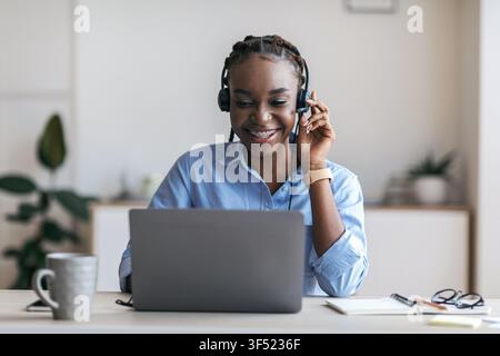 Black female manager wearing headset and using laptop in office, consulting client Stock Photo