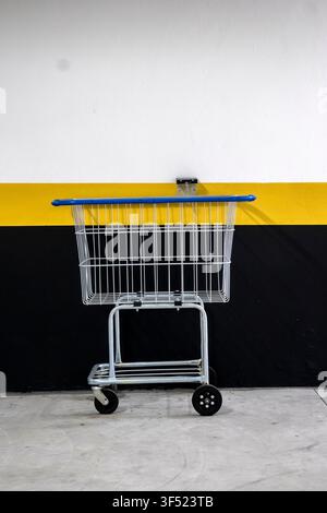 Empty metallic shopping cart parked against a yellow and black painted wall in an indoor garage or supermarket warehouse in Sao Paulo city. Stock Photo