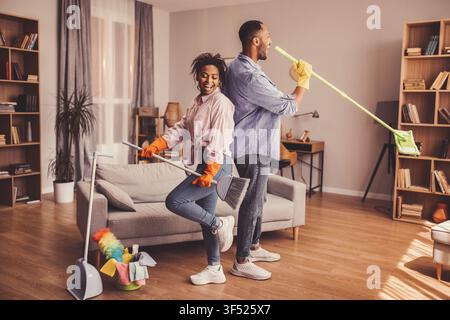 Happy Black Couple Cleaning Home Together, Dancing And Enjoying Household Chores Stock Photo
