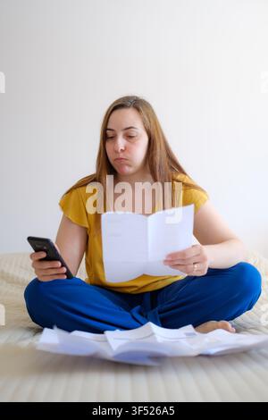 Woman analyzing documents and smartphone, dealing with debt and financial challenges Stock Photo