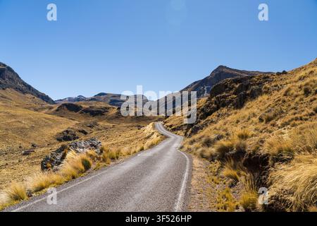 A winding paved road stretching through the vast and arid high-altitude mountain landscape of the Peruvian Altiplano under a clear blue sky Stock Photo