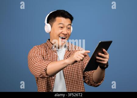 Happy Asian Male Listening To Music And Using Tablet At Home, Enjoying Technology Concept Stock Photo
