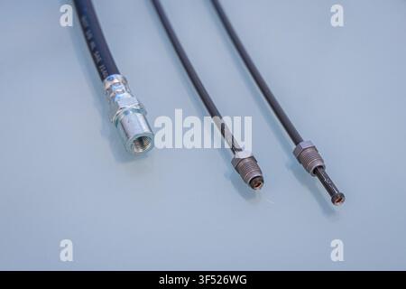 Three automotive brake lines lie on a light gray surface, showing a rubber hose with a threaded fitting on the left and two thin metal brake pipes Stock Photo