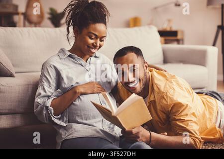 Happy African American Couple Reading Book Together At Home, Expecting Baby Stock Photo