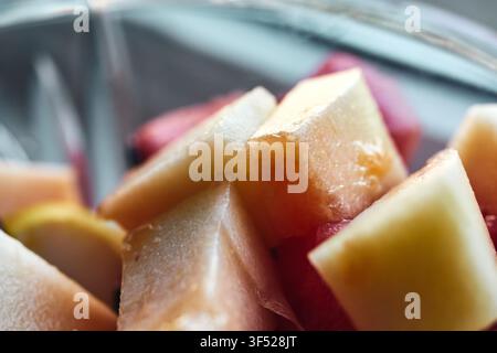 Macro close-up shot of fresh sliced fruit pieces, featuring juicy melon chunks and sweet tropical fruits prepared in a clear glass bowl for a healthy Stock Photo