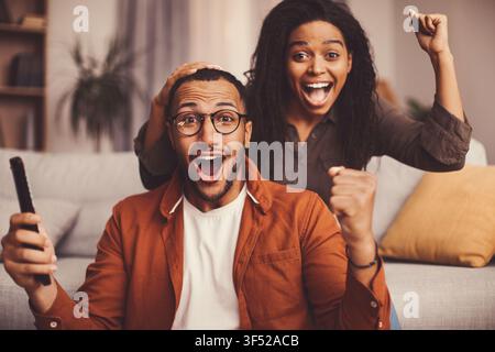 Excited African American Couple Celebrating Watching Television At Home Stock Photo