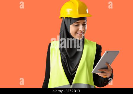 Female Muslim construction worker with tablet computer on orange background Stock Photo