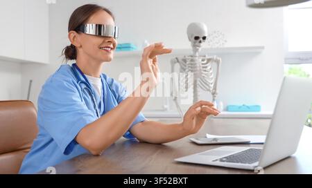 Female doctor in futuristic augmented reality glasses interacting with virtual interface in a modern medical office, She is dressed in blue scrubs wit Stock Photo