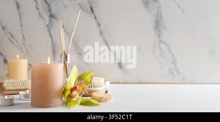 Spa treatment with burning candles, orchid flower, and bath accessories on a white table with marble background Stock Photo