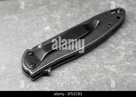 Closed folding pocket knife with pocket clip photographed in black and white, emphasizing metal texture, compact design and everyday carry utility for Stock Photo