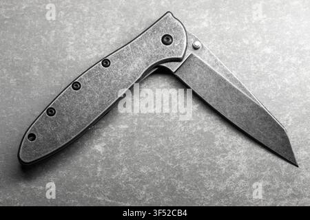 Close-up of a half opened folding pocket knife with a stonewashed blade and metal handle resting on a textured surface, conveying utility, craftsmansh Stock Photo