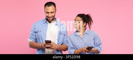 Happy Multiracial Couple Using Smartphones Together, Pink Background, Lifestyle Concept Stock Photo