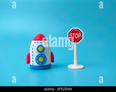A toy rocket positioned next to a miniature octagonal red stop sign on a blue background. Stock Photo