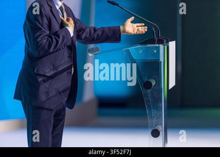 Business executive speaking at conference podium, gesturing during keynote presentation with microphones on stage. Ideal for leadership, communication Stock Photo